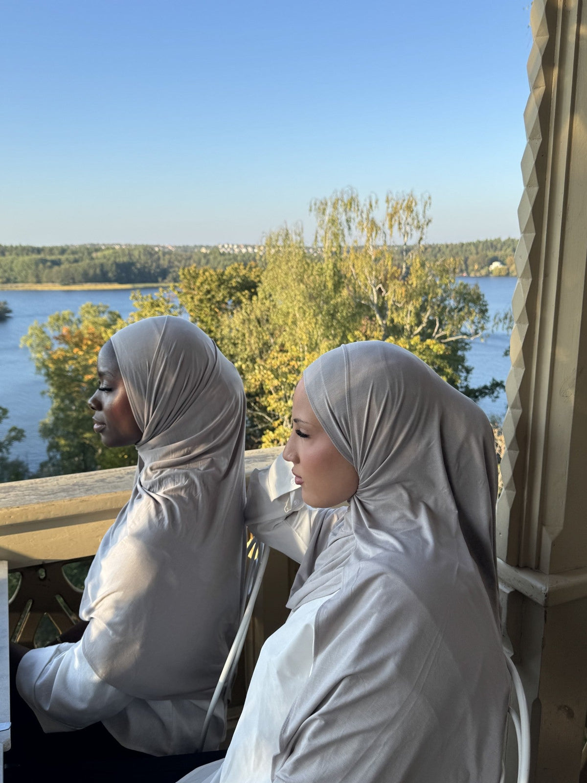 Two women in grey bamboo jersey hijabs on a balcony by a lake